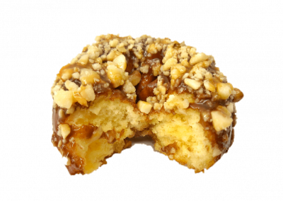 Chocolate glazed donut topped with macadamia nuts with a caramel drizzle from Purvé Donut Stop Hawaii with a bite missing showing the fluffy center