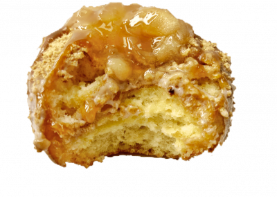 Fresh cinnamon and sugar donut topped with apple and caramel drizzle from Purvé Donut Stop Hawaii with a bite out of it showing the fluffy center